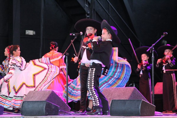 Students wearing mariachi clothing and Mexican dance dresses performing on stage 