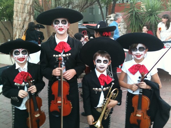 Students dressed in mariachi clothing with painted faces gathered together holding instruments. 