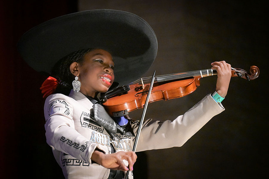 A young girl with braces smiles as she plays violin