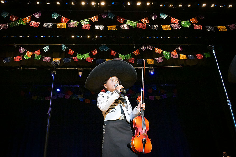 A young girl sings into a mic and holds her violin