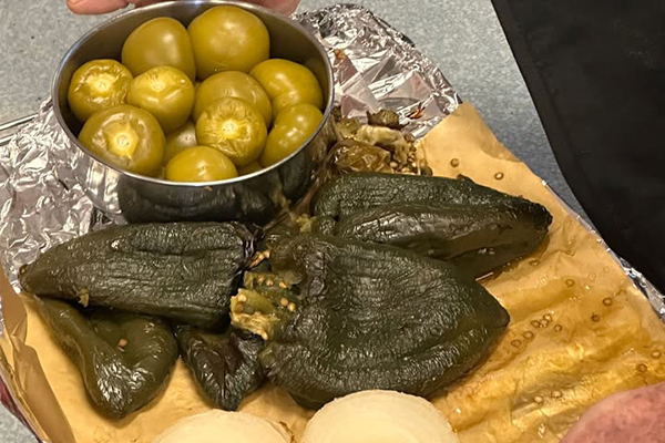 A bowl of tomatillos and roasted peppers on a cutting board