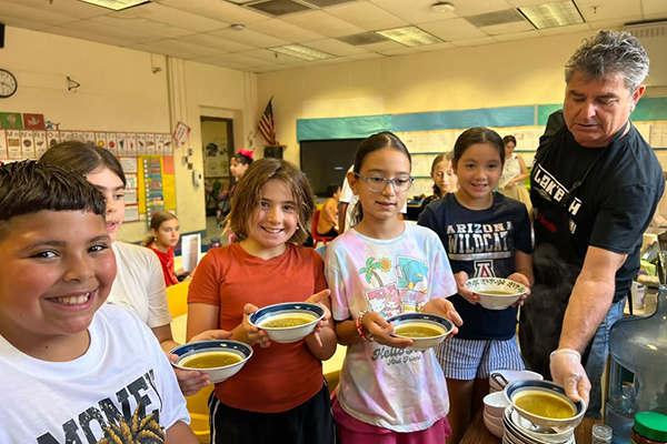 A group of students smile holding up their bowls of soup