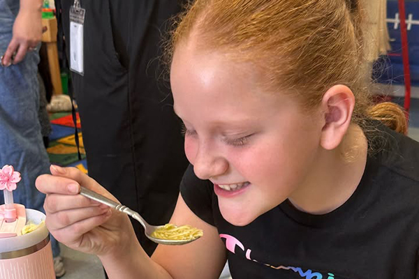 A girl smiles as she enjoys her bowl of sopita de fideo