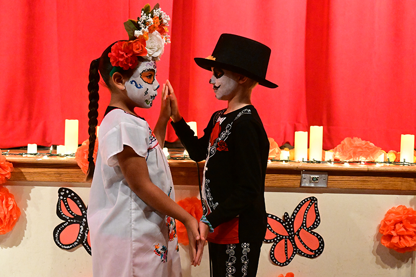 A girl and boy in Dia de los Muertos attire and makeup dance together