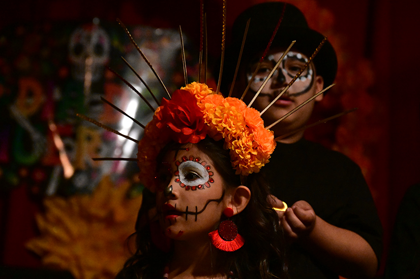 A girl in an orange spiky floral headpiece and Dia de los Muertos makeup