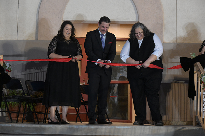 Two women and a man cut a red ribbon