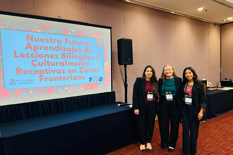 Three women smile next to a presentation screen
