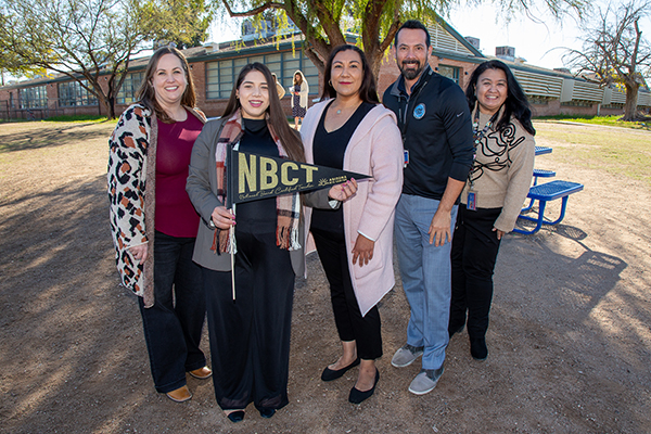 A woman, second from left, holds an NBCT pennant surrounded by her colleagues