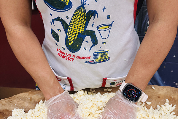 A woman in a corn apron mixes masa by hand