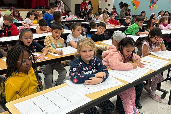 Students sitting at tables write on pieces of paper
