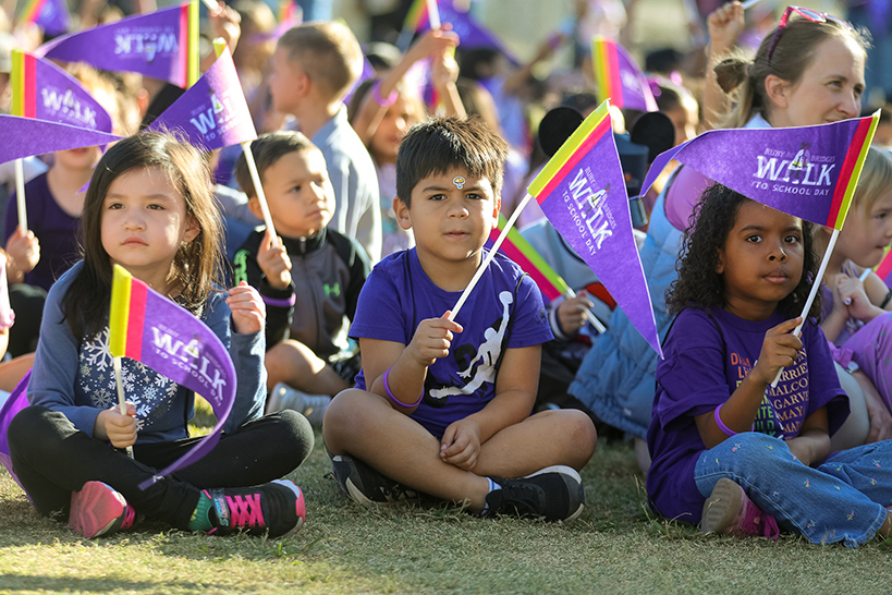 Students sit on the grass, holding up their purple Ruby Bridges pennants