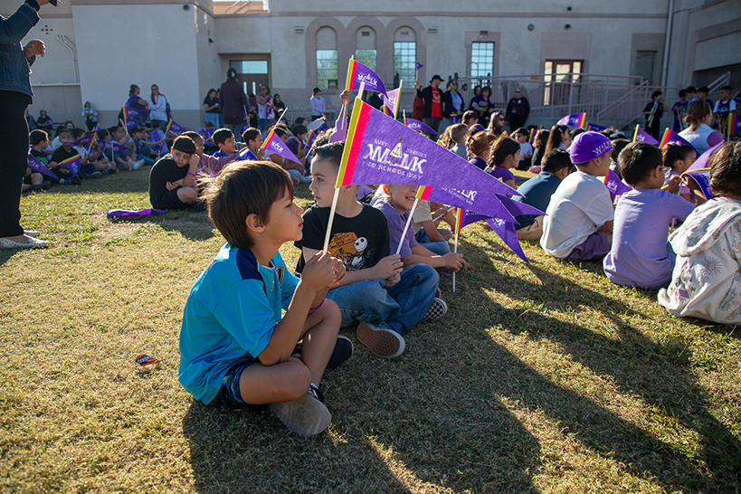 Students sit on the grass, holding their purple Ruby Bridges pennants