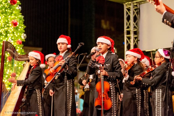 Students wearing mariachi clothing and Santa hats playing instruments while preforming on stage