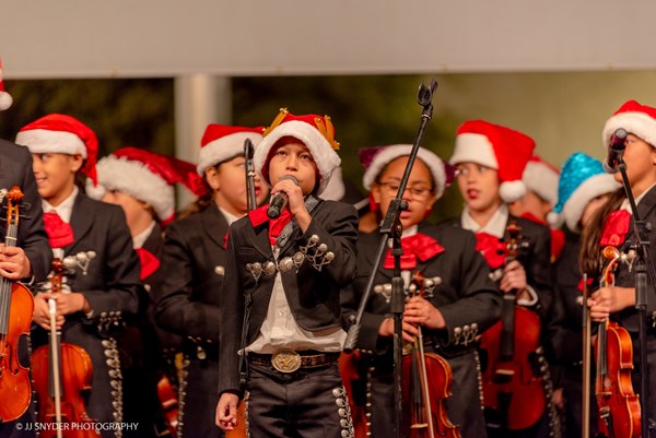 Students dressed in mariachi clothing and Santa hats preforming on stage 