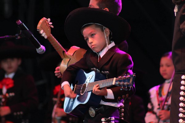 Students wearing mariachi clothing, playing guitars while performing on stage