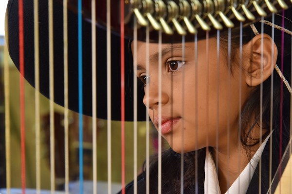 Student dressed in mariachi clothing gazing through strings on a harp