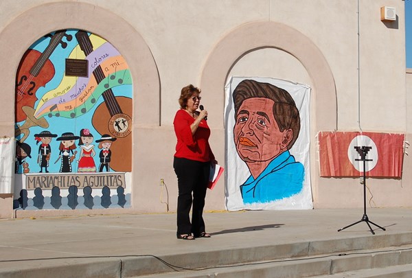 Teacher standing in front of murals and paintings making an announcement in a microphone 