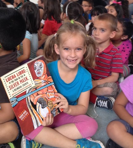 Student sitting in crowd holding a Lucha Libre book while smiling