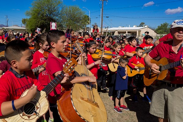 A very large group of students and teachers gathered together playing instruments and singing