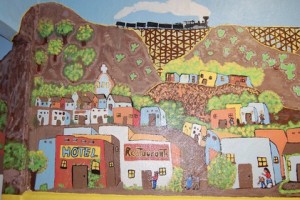 Mural of colorful pueblo-style houses in mountains and a train on a train track bridge