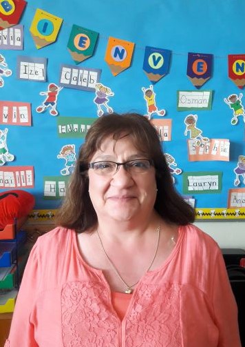 Kindergarten Teacher Alma Armendariz smiling in her classroom in front of a wall of childrens' projects
