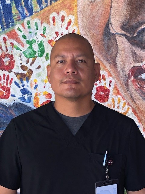 Efren Peralta, Health Clerk standing in front of a colorful mural