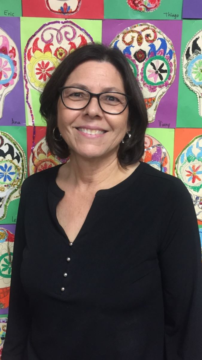 Librarian Mercedes Vella smiles with an illustration of colorful Mexican skulls behind her